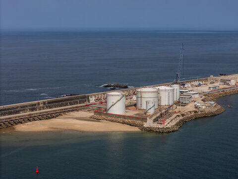 Aerial view of LNG silos situated on a breakwater along the Atlantic coast with a crane and calm sea in Matosinhos, Porto, Portugal.
