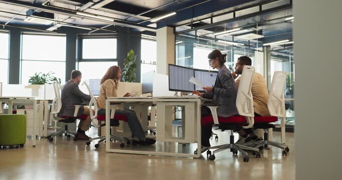 Team analysts accountants in office with computers. Professionals review data charts and business reports in a bright modern open plan workplace. Strong concept of teamwork and analysis.