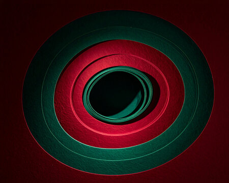 Paper circles in red and green build a tunnel structure. Shadows add depth to the center. Color contrast highlights geometry and form. Layers create background space for design. Craft composition art.