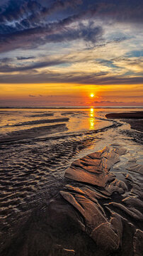 Golden sunset over the ocean coast with dramatic cloudy sky and wet sandy textures.