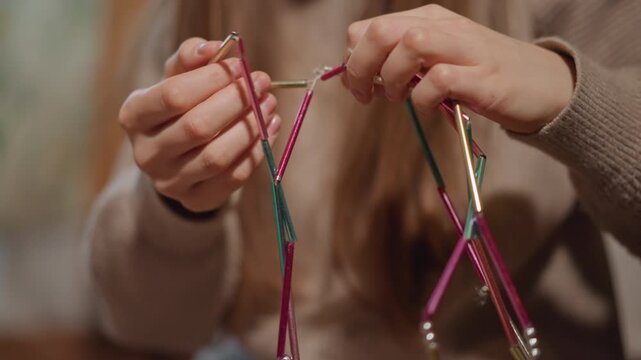 Detailed craft demonstration. Woman creating colorful beaded garland. Closeup of hands making decorative strings. Woman in sweater carefully arranging beads on colorful garland indoors