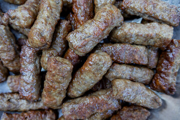 Fototapeta premium Freshly cooked cevapi piled together in a metal tray, captured in close detail with browned edges and a rustic texture, representing traditional Balkan grilled meat cuisine.