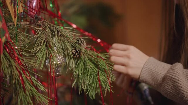 Festive woman embellishing pine branches. Woman adding holiday ornaments to pine branches scene. Interior setting captures woman beautifying pine branches with festive decorations in cozy atmosphere