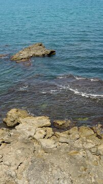 Vertical view of large rock formation in turquoise sea water near rocky limestone coastline on a clear day