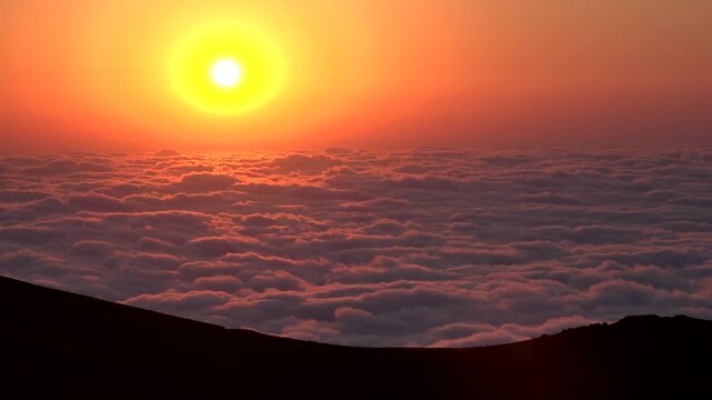 Timelapse sunset glows above sea of clouds, pink sky, and mountain silhouette at dusk.