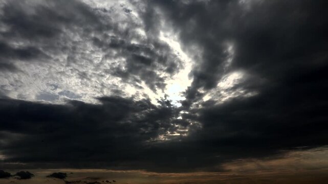 Sunset light breaks through dark storm clouds after rain creating dramatic timelapse sky scene.