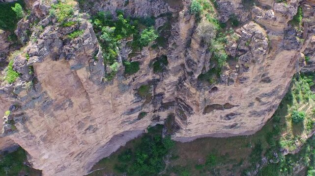 Aerial view reveals vertical karst cliff, limestone wall, and eroded rock layers near canyon.
