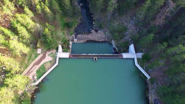 Aerial view of a small forest dam with a calm reservoir and controlled drainage.