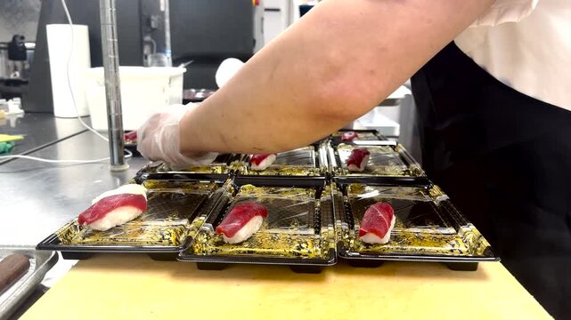 High-quality 4K stock footage showcasing rows of fresh tuna sushi nigiri and maki rolls beautifully arranged on black and gold retail trays in a commercial setting.
