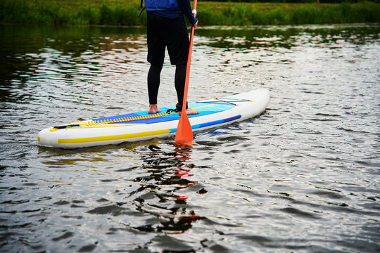 Individual practicing stand up paddleboarding in nature. Solo paddler wearing a life jacket balancing on an inflatable SUP board on a quiet lake surface during summer.