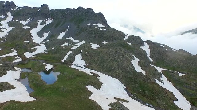 Aerial view of alpine mountain lake surrounded by melting spring snow and rugged peaks.