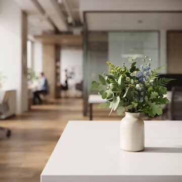 A simple yet elegant vase of greenery and blue flowers sits on a clean white table, with the soft blur of a modern office environment in the background, creating a serene and professional atmosphere.