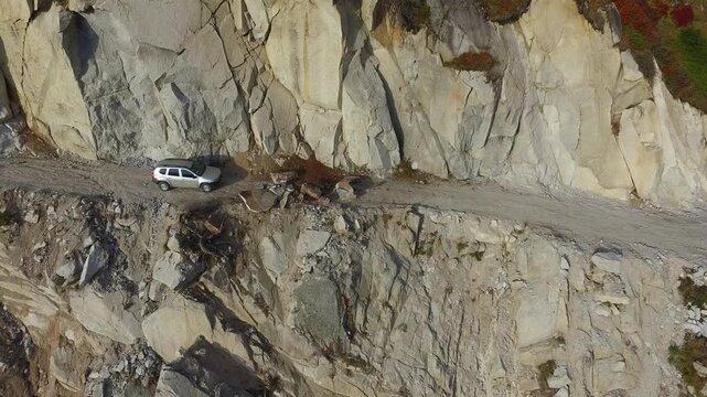 Aerial view of stranded 4x4 SUV on dangerous mountain road blocked by landslide near cliff.