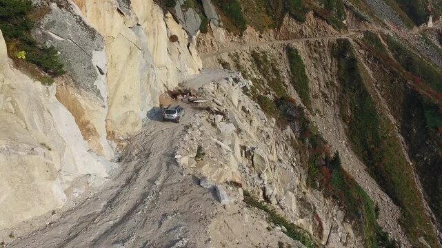 Aerial view of stranded 4x4 SUV on dangerous mountain road blocked by landslide near cliff.