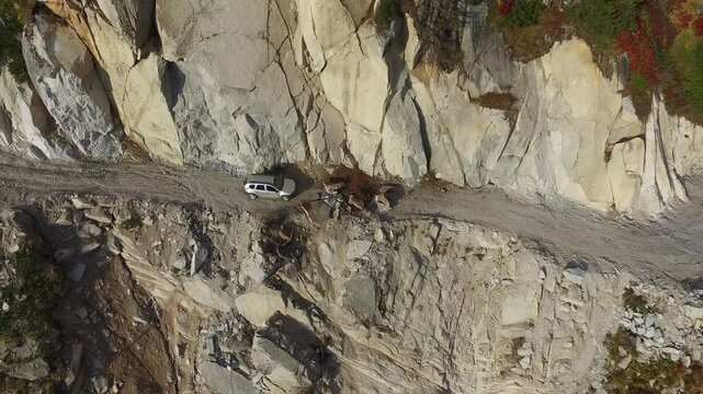 Aerial view of stranded 4x4 SUV on dangerous mountain road blocked by landslide near cliff.