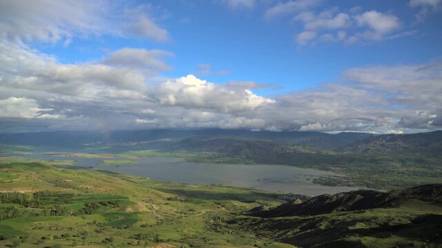 Variable weather clouds over lake surrounded by green meadows in Sivas Turkey countryside.