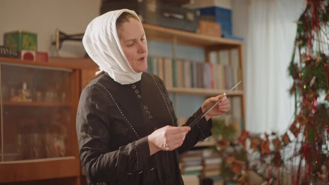Elderly woman in headscarf inspecting vinyl, cozy parlor setting with wooden cabinet, bookshelf and garland, handling album sleeve and disc with gentle hands, measuring tape and notebook