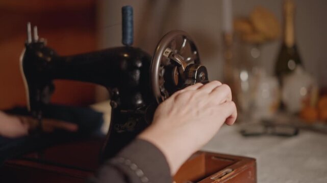 Woman sews diligently. An individual skillfully operates vintage machine during evening hours. Sewing enthusiast precisely guides fabric through classic sewing machine under gentle ambient lighting