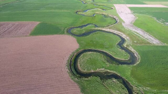 Aerial view of river meander flowing through agricultural fields on a flat plain in France.