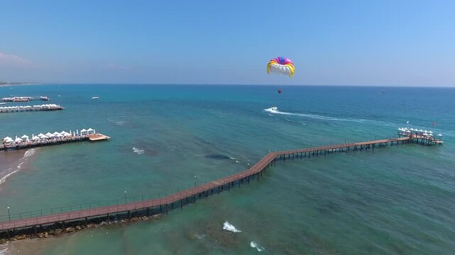 Aerial view of summer vacation tourists parasailing behind Revival boat near hotel pier.