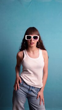 Young woman wearing sunglasses dancing against a blue background