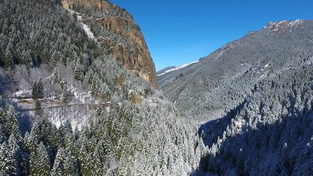 Aerial drone view captures snow covered Sumela Monastery clinging to steep rocky mountain cliff.