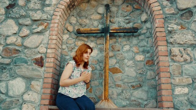 A woman prays silently and religiously before a Christian crucifix in Italy