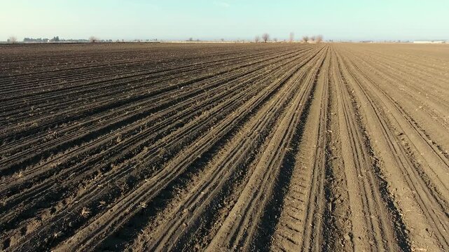 Aerial view of blue tractor sowing seeds across wide flat brown agricultural plain landscape.