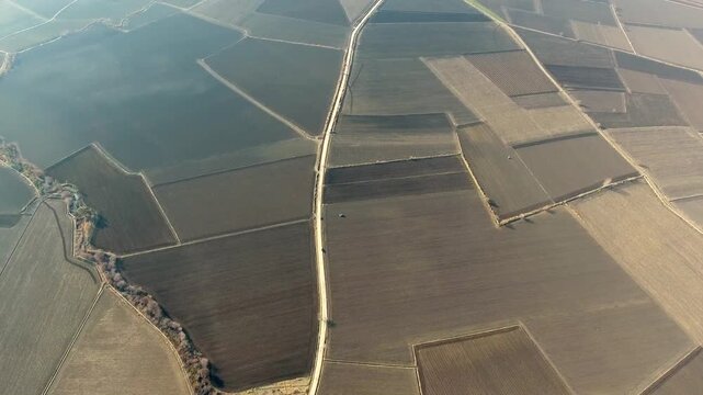 Aerial view of village houses and dirt field roads across flat brown alluvial plain.