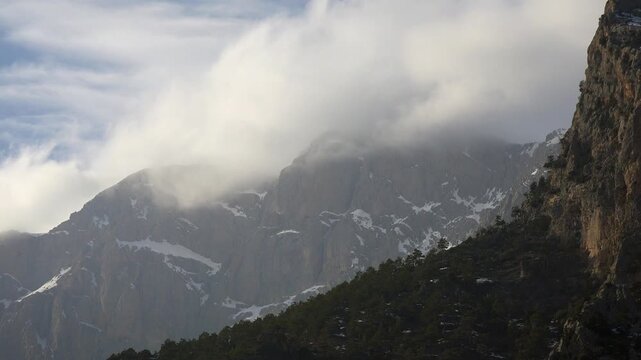 Rocky peak rising through clouds on snowy high mountain wall in the Rocky Mountains of America.