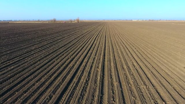 Aerial view of uncultivated plowed brown field with parallel furrows in agriculture.
