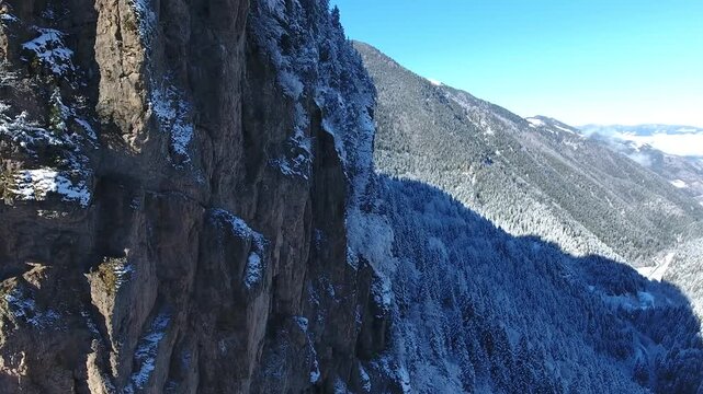 Aerial drone view captures snow covered Sumela Monastery clinging to steep rocky mountain cliff.