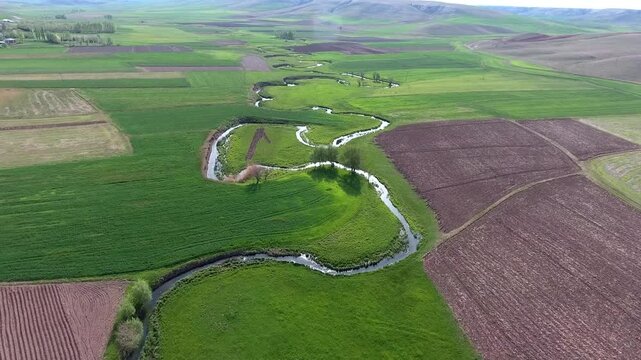 Aerial view of meandering river curving through green fields across flat rural plain landscape.