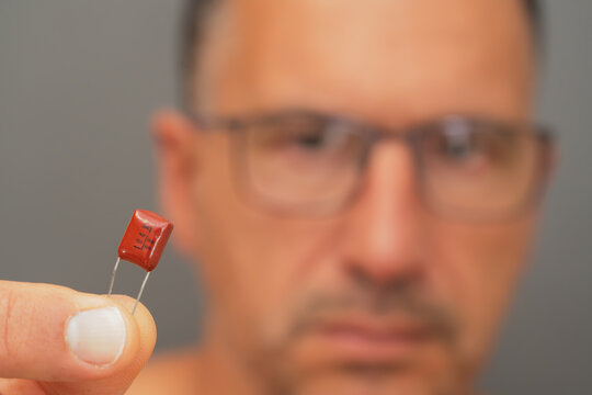 A male electrical engineer observes a polyester capacitor.