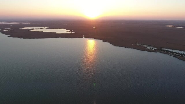 Aerial sunrise over still lake surrounded by reeds in vast northern wetland landscape.