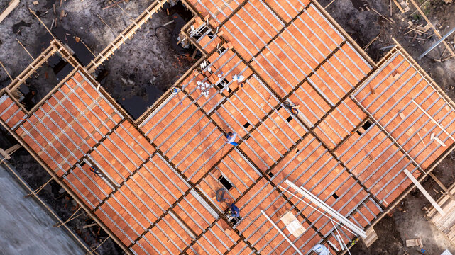 Aerial view of a residential construction site featuring workers installing pre-cast concrete beams and clay tiles for a new house in Florianopolis, Santa Catarina, Brazil.
