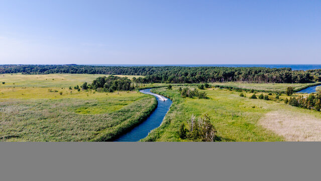 Aerial view of jet ski cruising along winding river surrounded by green meadows and forest