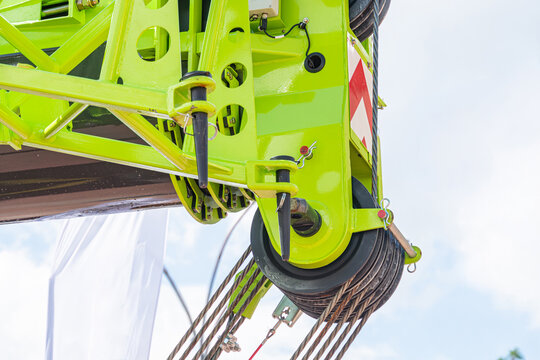 Close-up view of a mobile crane boom head painted in bright lime green, highlighting the heavy-duty pulley block assembly. The setup shows multiple steel wire ropes routed through the pulleys,