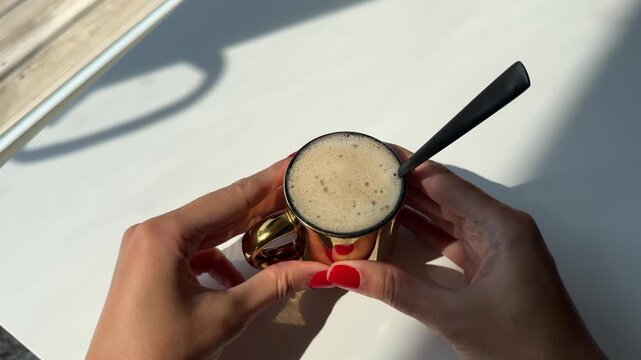 4K horizontal close-up video of a woman's hand with red manicure gently stirring creamy white foam in a cup of freshly brewed coffee against a clean white background. Minimalist coffee and lifestyle 