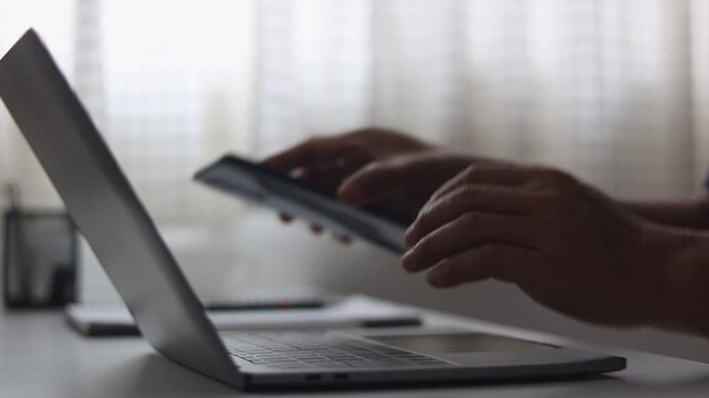 Close-up of a man's hands using two-factor authentication with a smartphone and a laptop, showing data security, login and password protection online. Cybersecurity, Cyber security 2FA login concept.