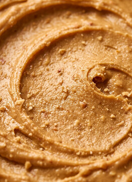 Macro close-up view of chunky peanut butter texture with a circular swirl pattern and crushed nut pieces