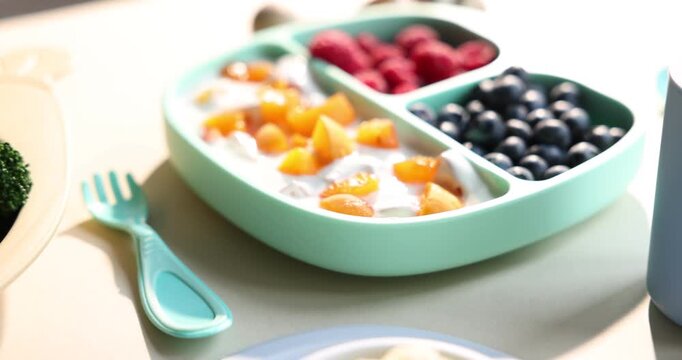Baby tableware. Section plates with food and cutlery on white table, closeup. Camera moving up
