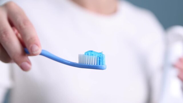 Woman applying toothpaste on toothbrush against blue background, closeup