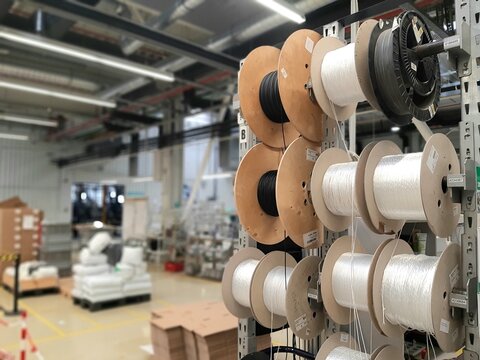 Industrial cable reels and spools with electric wire stored on rack shelves in factory warehouse. Optical fiber reels, wiring components manufacturing and industrial electrical equipment concept.
