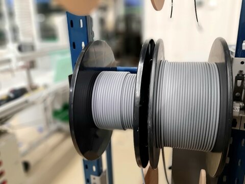 Industrial cable reels and spools with electric wire stored on rack shelves in factory warehouse. Optical fiber reels, wiring components manufacturing and industrial electrical equipment concept.