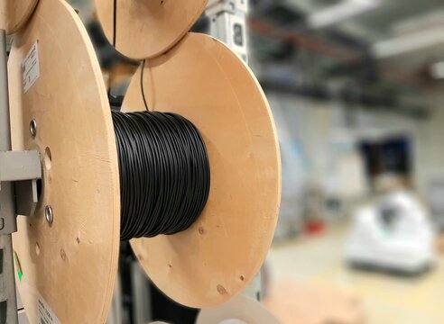 Industrial cable reels and spools with electric wire stored on rack shelves in factory warehouse. Optical fiber reels, wiring components manufacturing and industrial electrical equipment concept.
