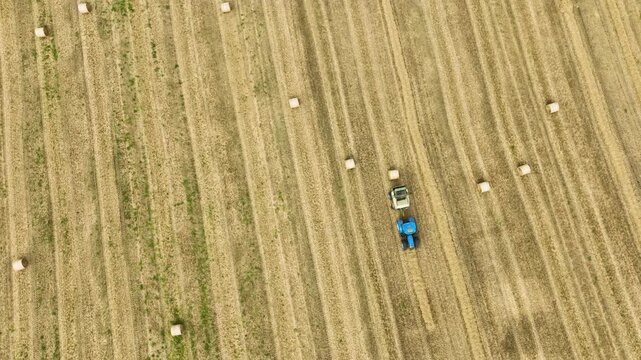 Tractor towing round baler through stubble field with scattered bales