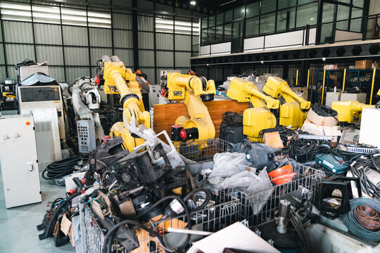 Industrial robot robotic arm factory machinery automation workshop equipment metal yellow robotic arm in cluttered factory warehouse with cable tool part and control cabinet