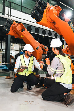 Industrial robot engineer factory worker safety helmet robotic arm automation maintenance inspection manufacturing engineers reflective vest inspect orange robotic arm machinery inside modern