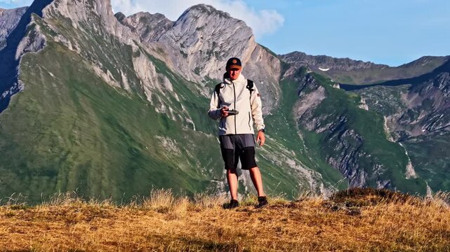 Aerial close up reveal shows hiker standing on grassy ridge flying drone with dramatic Pyrenees mountains behind at Col d'Aubisque